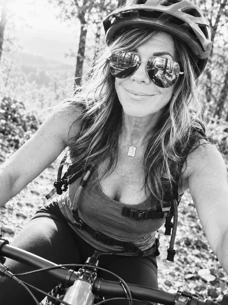 Lisa smiling in a bike helmet and sunglasses on a mountain trail at sunset