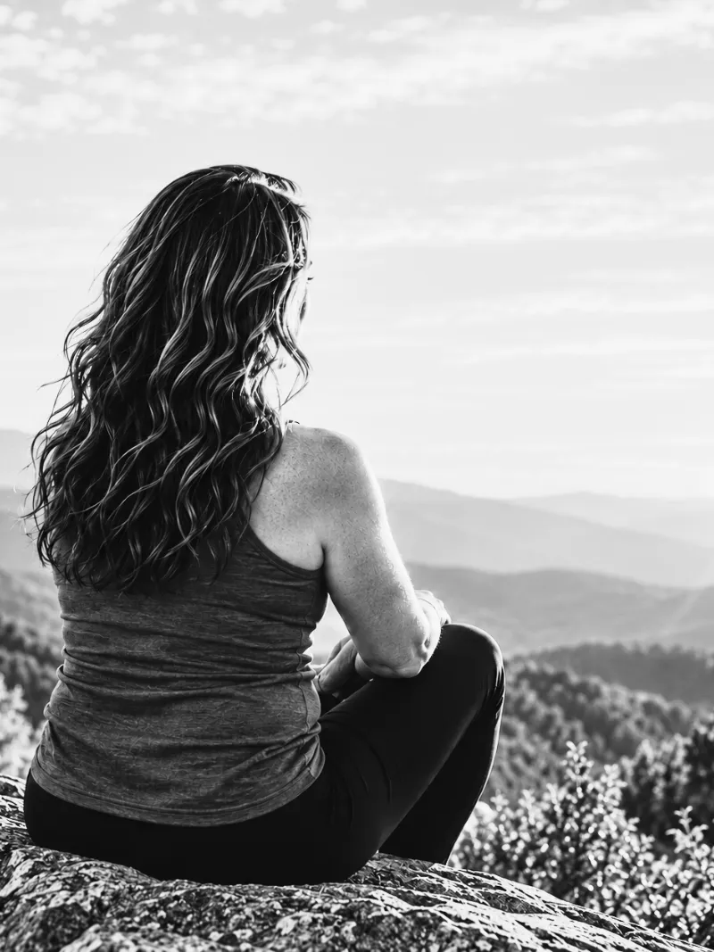Lisa sitting on a rock ledge, looking out over layers of mountains
